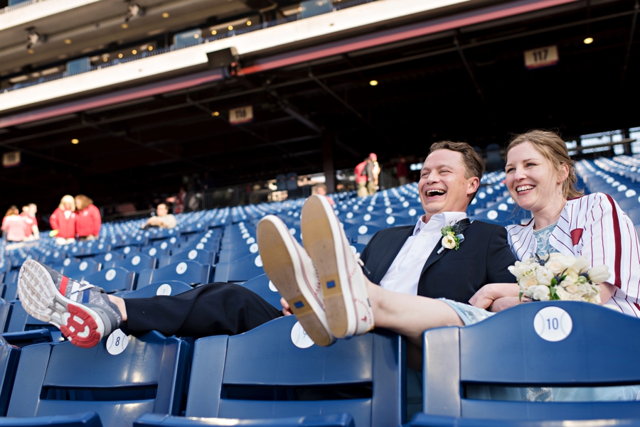 A bride and groom laugh and relax in the seats at a Phillies game on their wedding day.